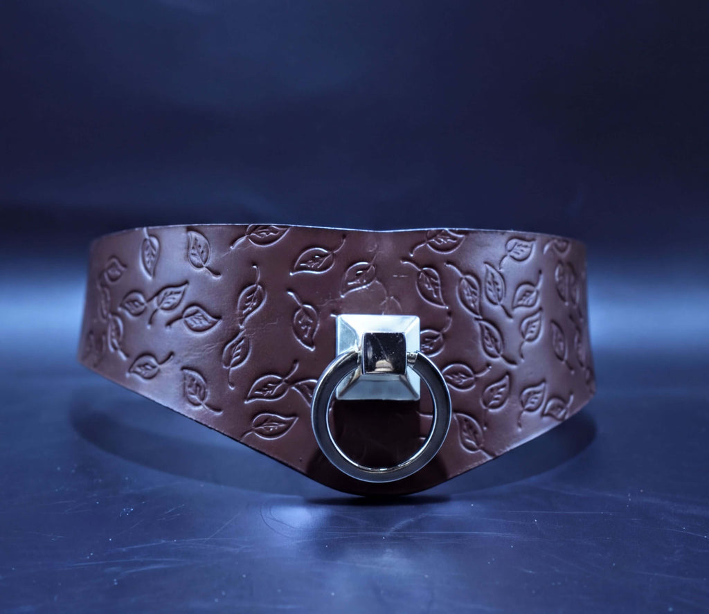 A brown leather choker necklace with a metal ring and leaf pattern design.