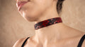 A close-up of a woman's neck and chest area wearing a red and black choker necklace.