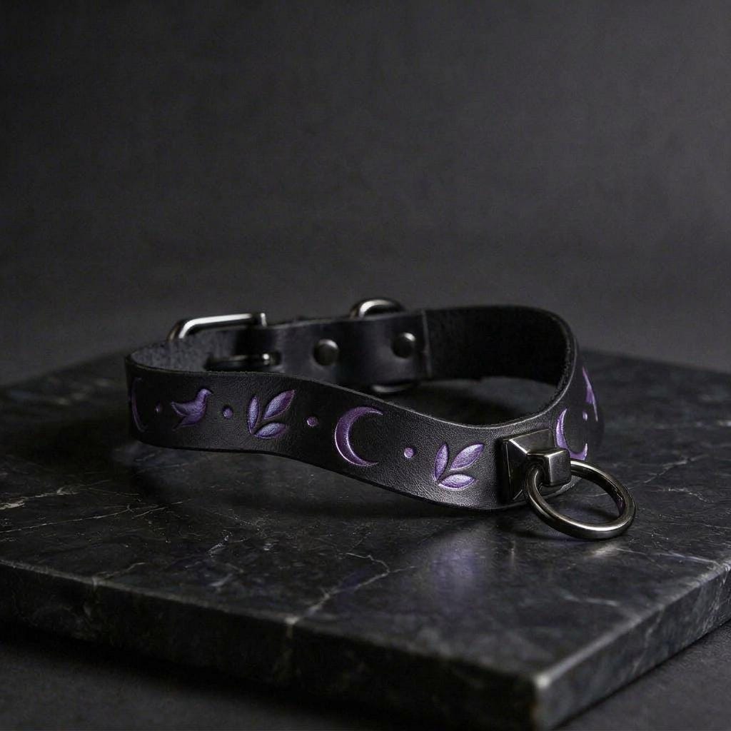A black leather choker necklace with purple floral designs and a metal ring on the front, resting on a dark surface.