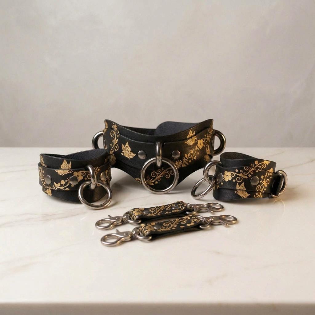 A set of black leather straps with gold floral designs, arranged on a white marble surface.