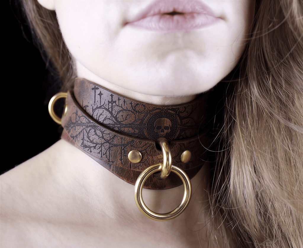 A close-up of a woman's neck and chin wearing a brown leather choker necklace with a skull design and a gold ring.
