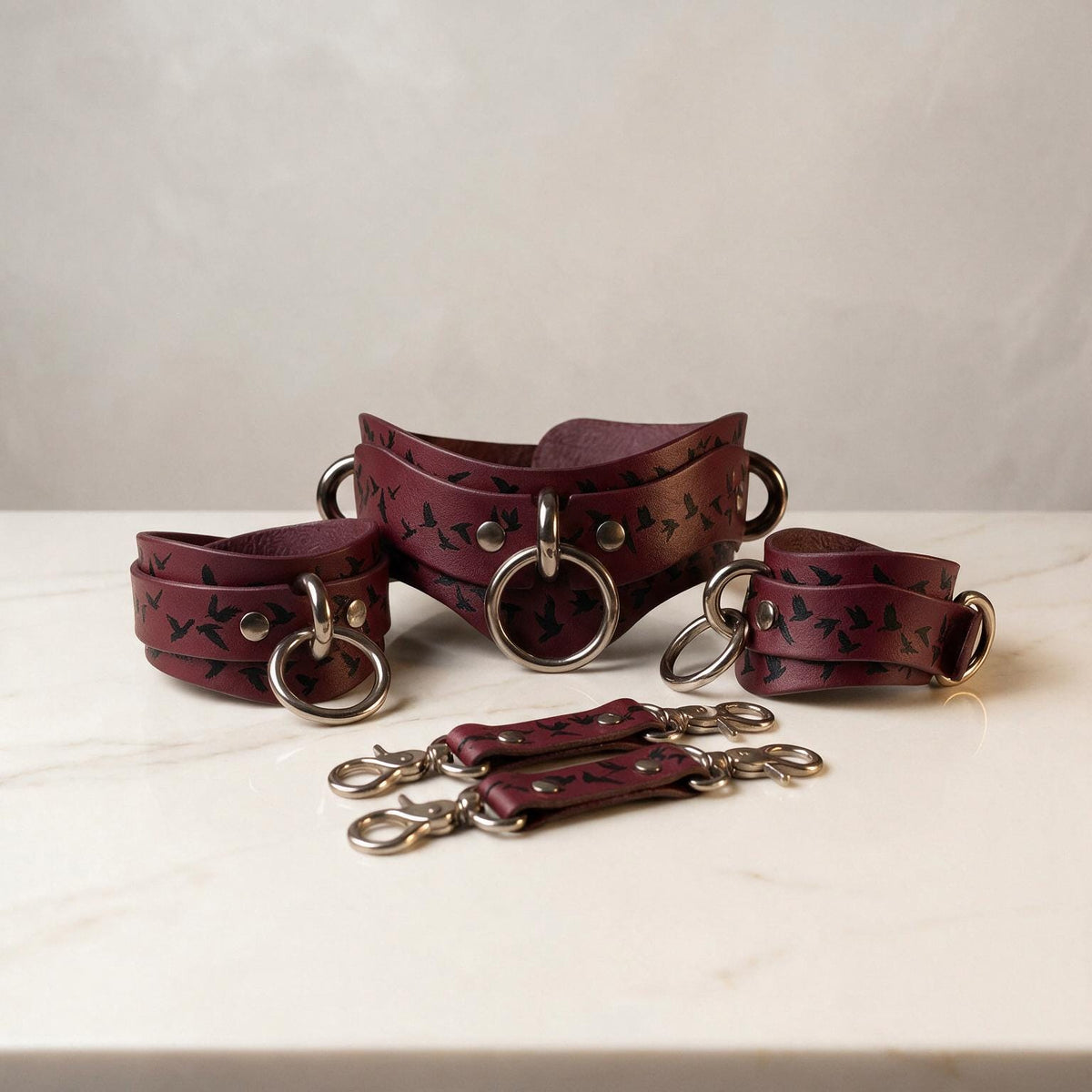 a collection of burgundy leather straps with metal rings and buckles, arranged on a white marble surface.