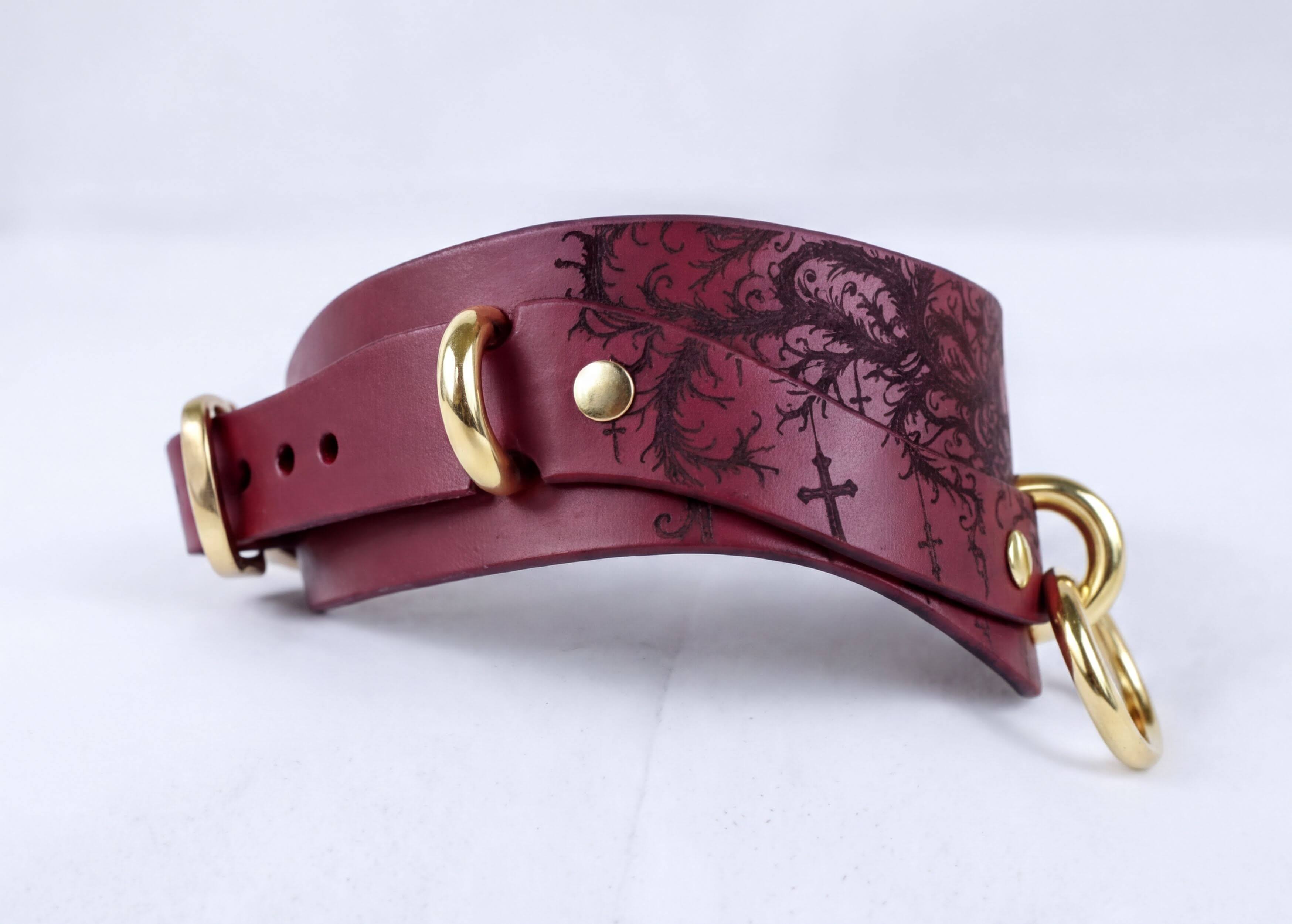A burgundy leather choker collar with a decorative pattern and gold hardware.