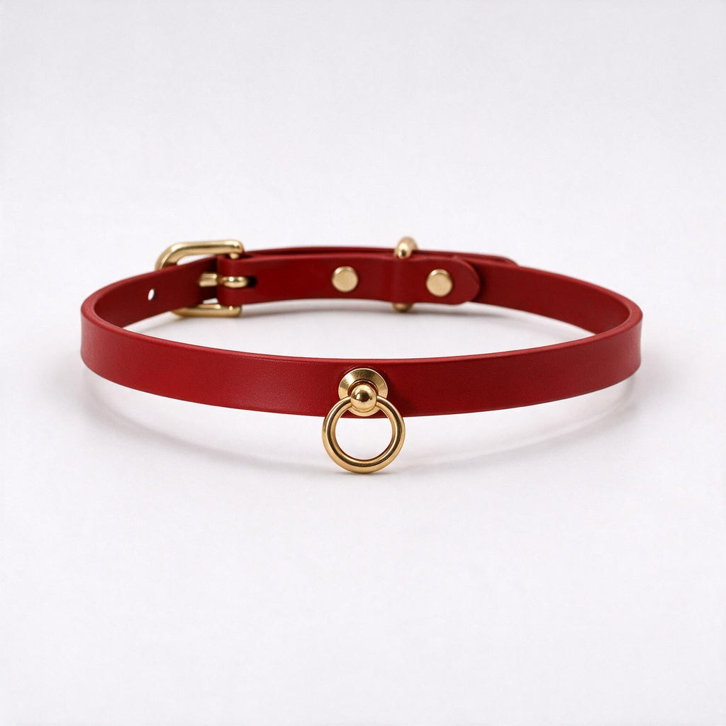 A red leather choker collar with a gold metal ring and buckle.