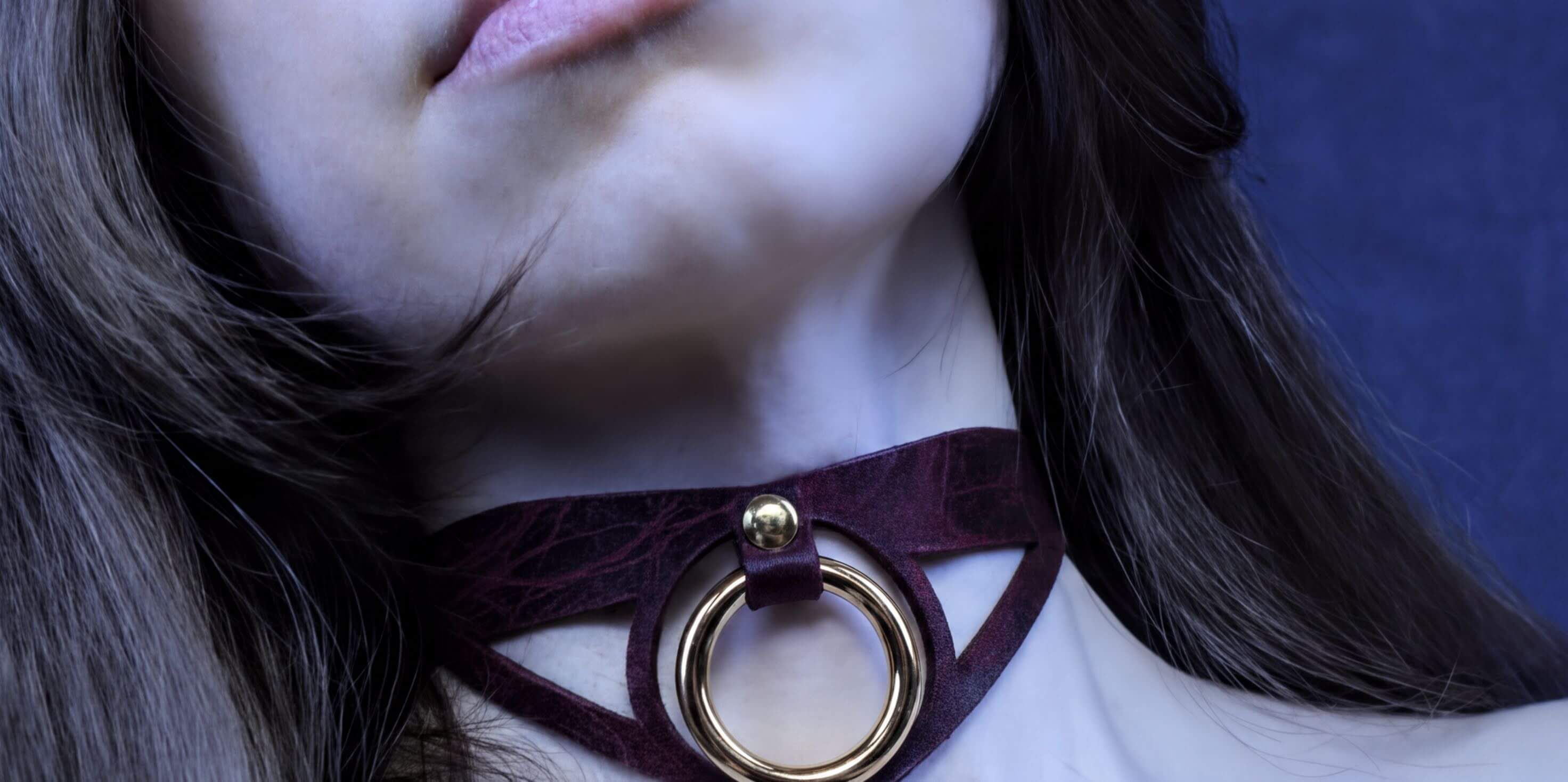 A close-up of a woman's neck and chin wearing a burgundy choker necklace with a gold ring.