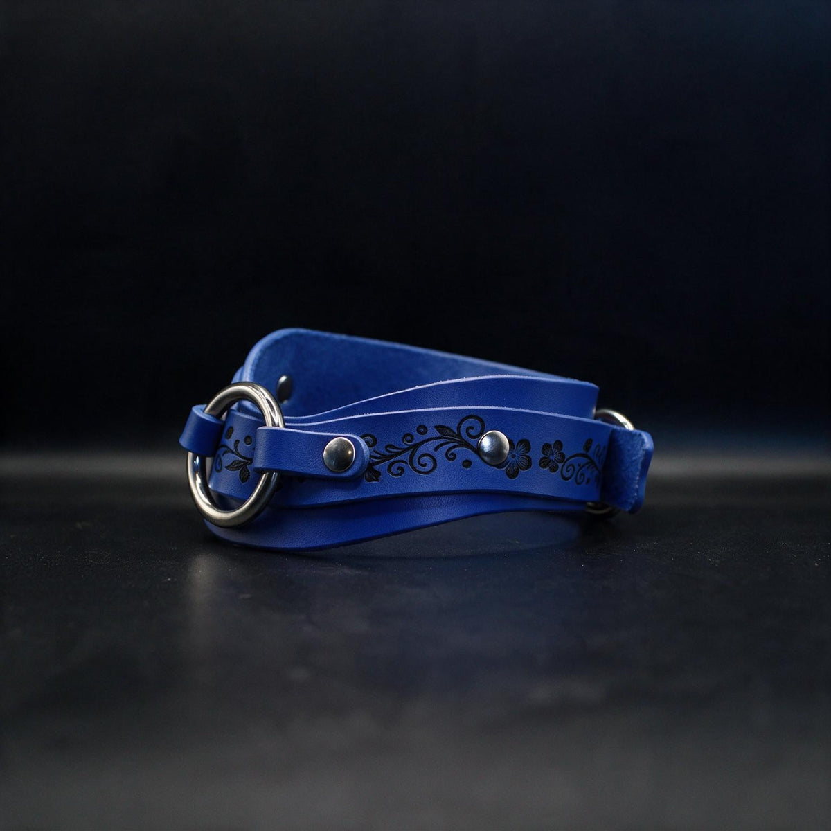 A blue leather belt with a floral design on it, resting on a dark surface.