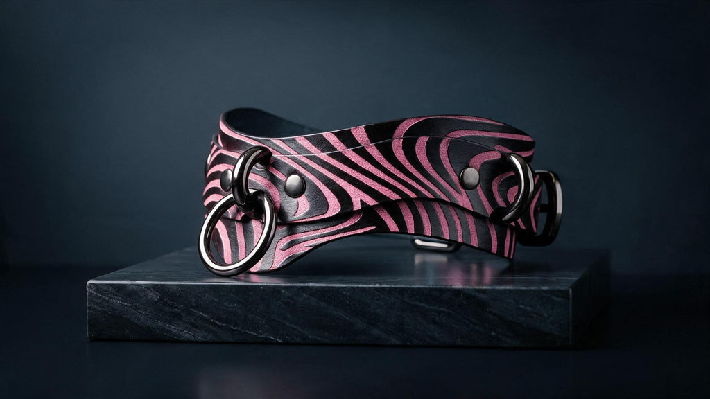 A zebra-striped leather collar with metal rings is displayed on a black marble pedestal against a dark background.