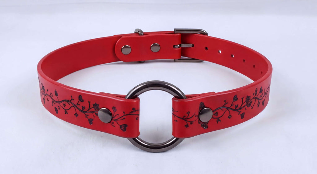 A red leather choker necklace with a metal ring and decorative floral pattern.