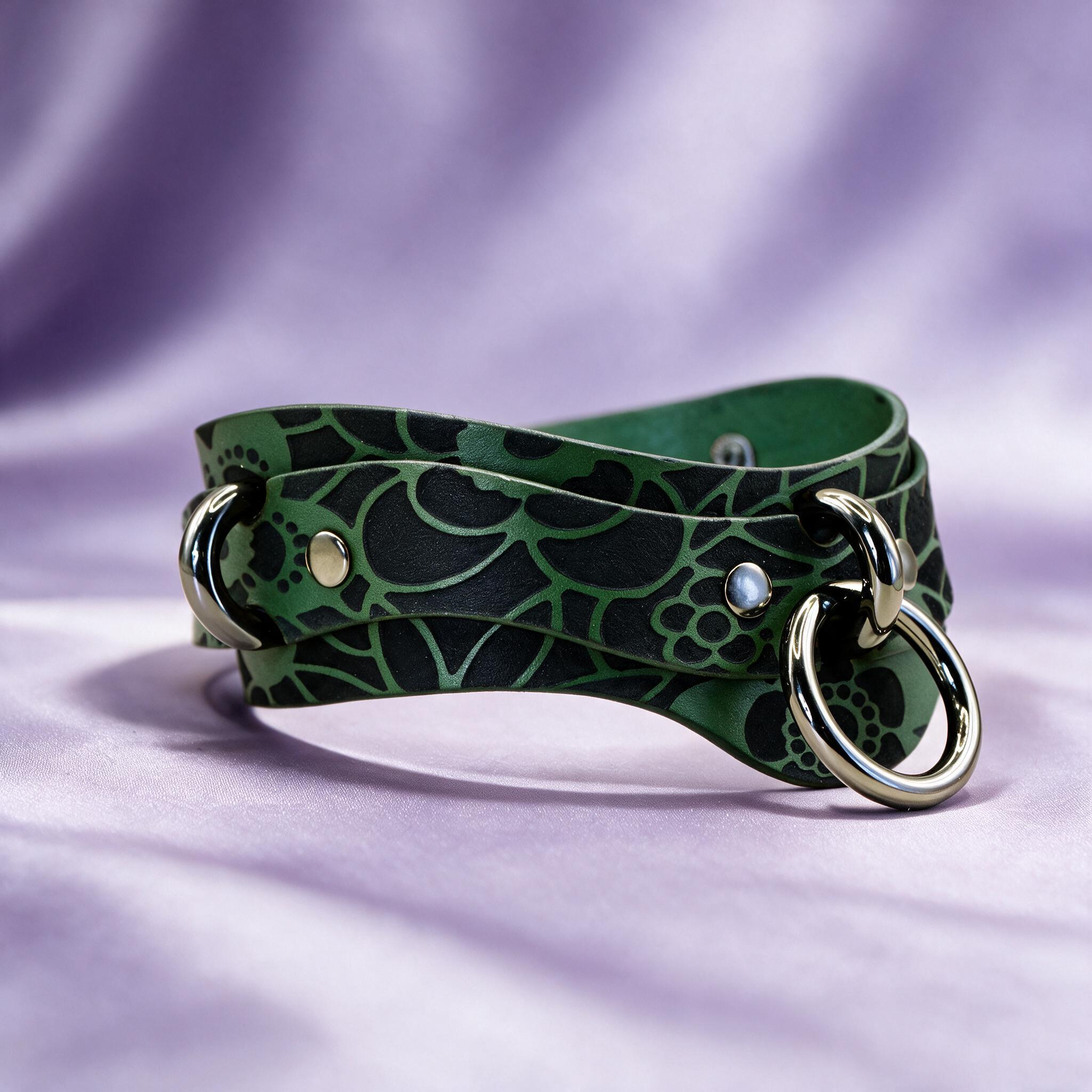 A green leather choker necklace with a floral pattern and metal rings on the ends, resting on a purple background.