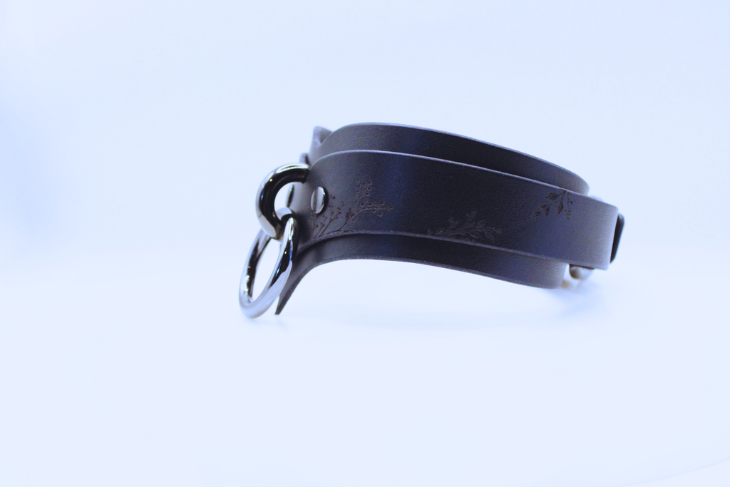 A black leather choker necklace with a metal clasp and a floral design on the clasp.