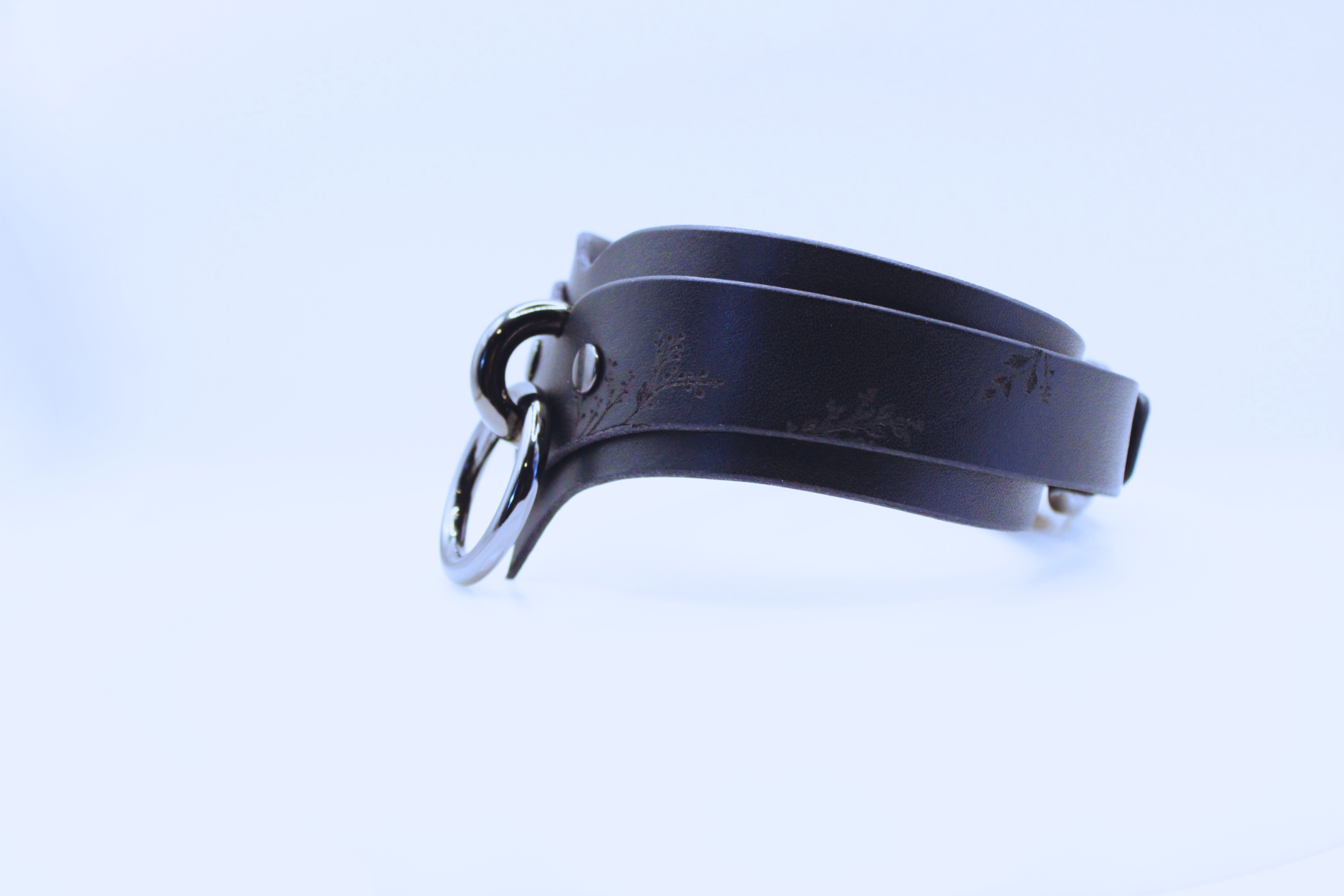A black leather choker necklace with a metal clasp and a floral design on the clasp.