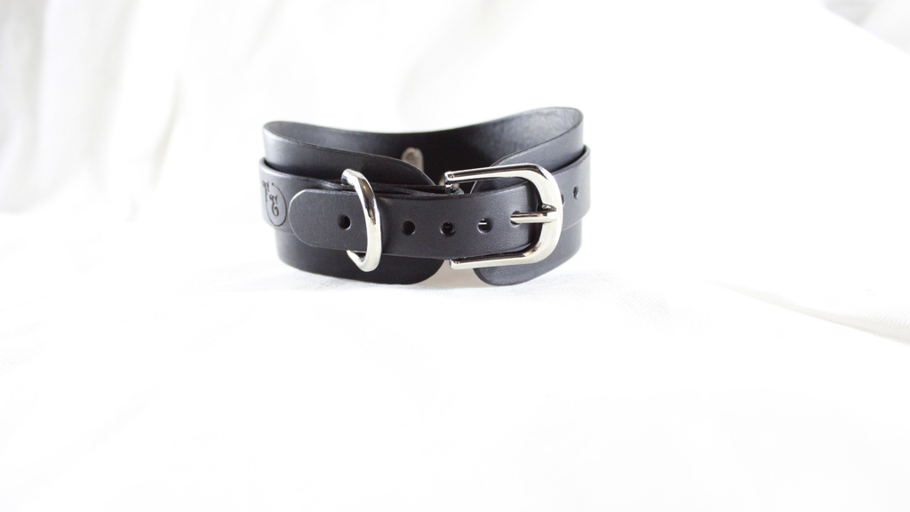 A black leather belt with a silver buckle is shown against a white background.