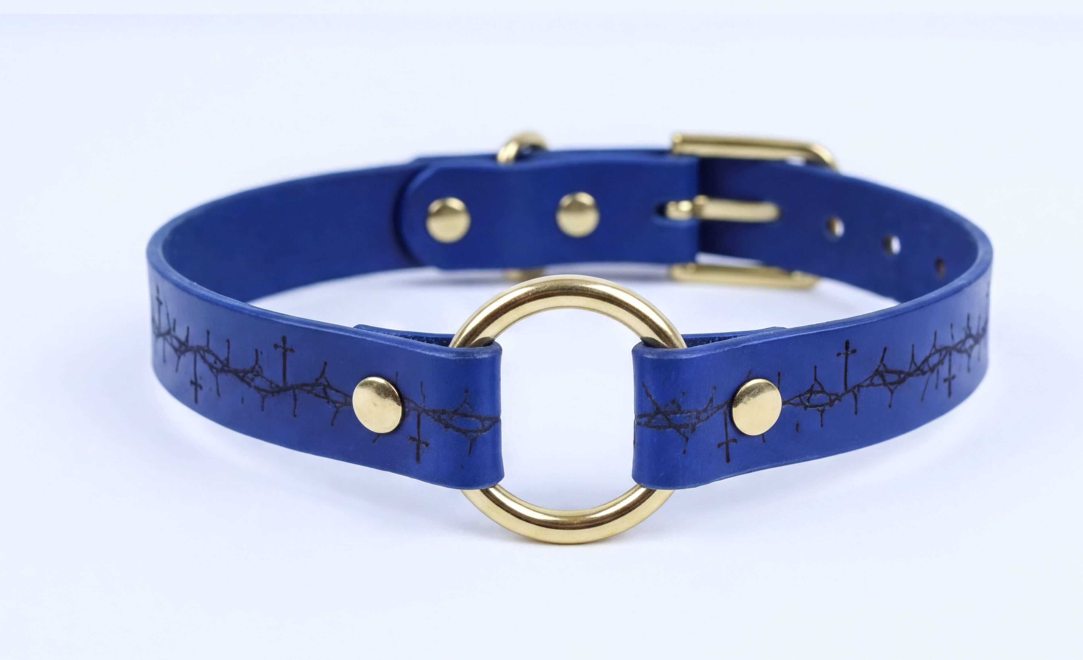 A blue leather choker collar with a gold ring and a black design on the front.