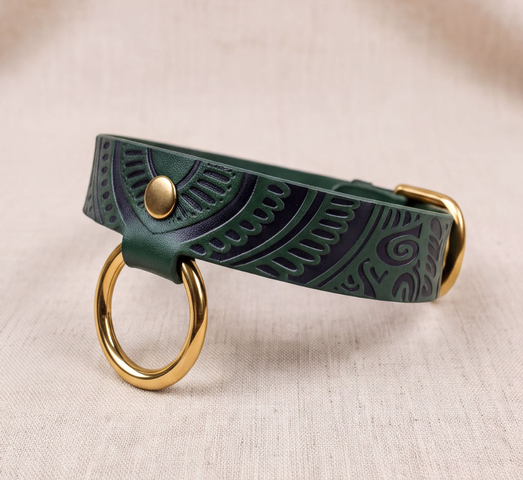 A green leather dog collar with a gold ring and buckle, placed on a beige background.