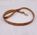A brown leather leash with a gold-colored metal clasp and a heart-shaped charm attached.