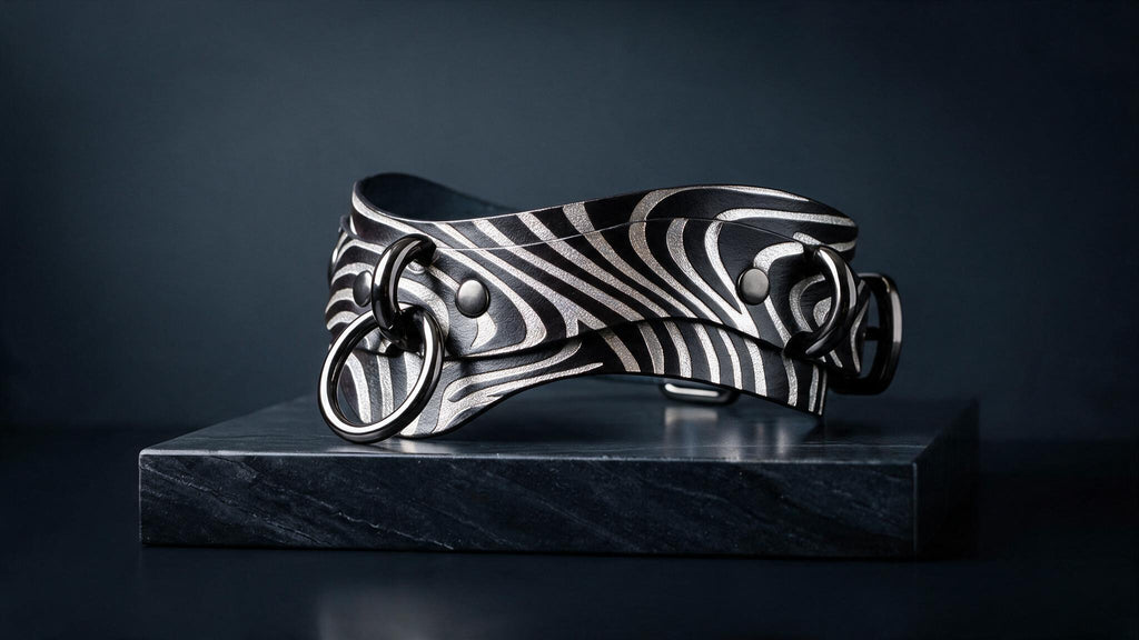 A zebra-striped leather choker necklace with metal rings and a metal buckle is displayed on a black marble pedestal against a dark background.