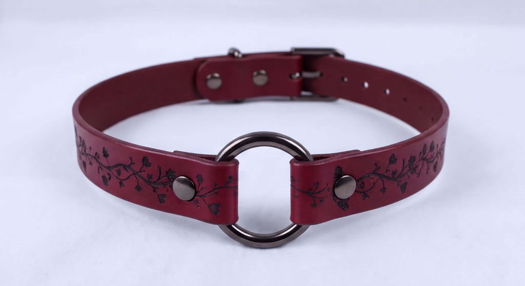 A burgundy leather choker necklace with a metal ring and decorative floral patterns.
