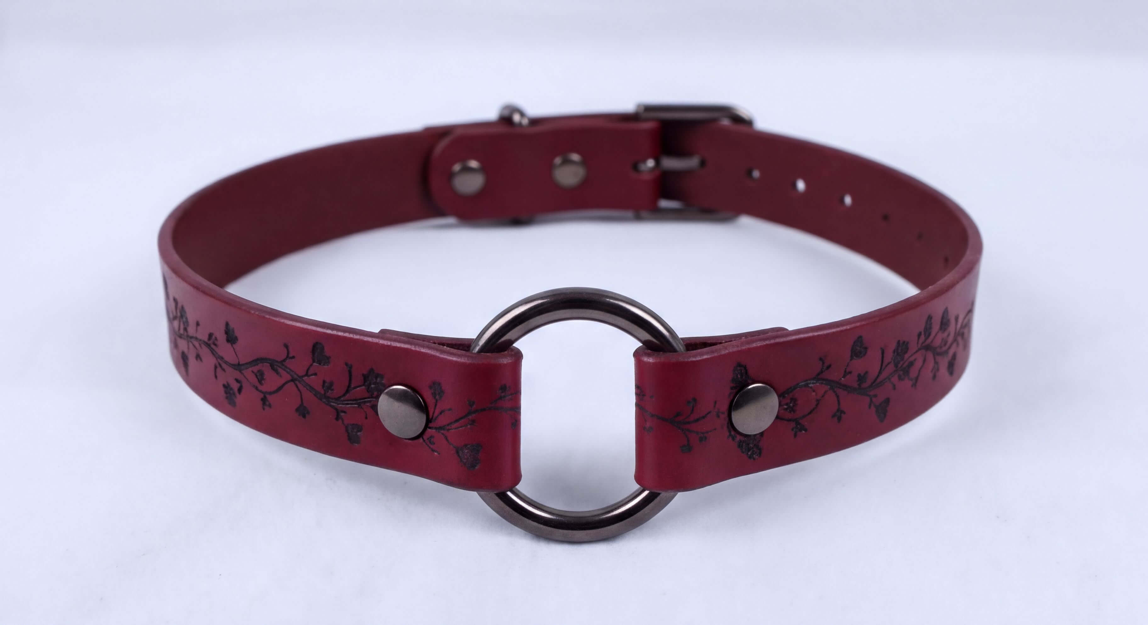 A burgundy leather choker necklace with a metal ring and decorative floral patterns.