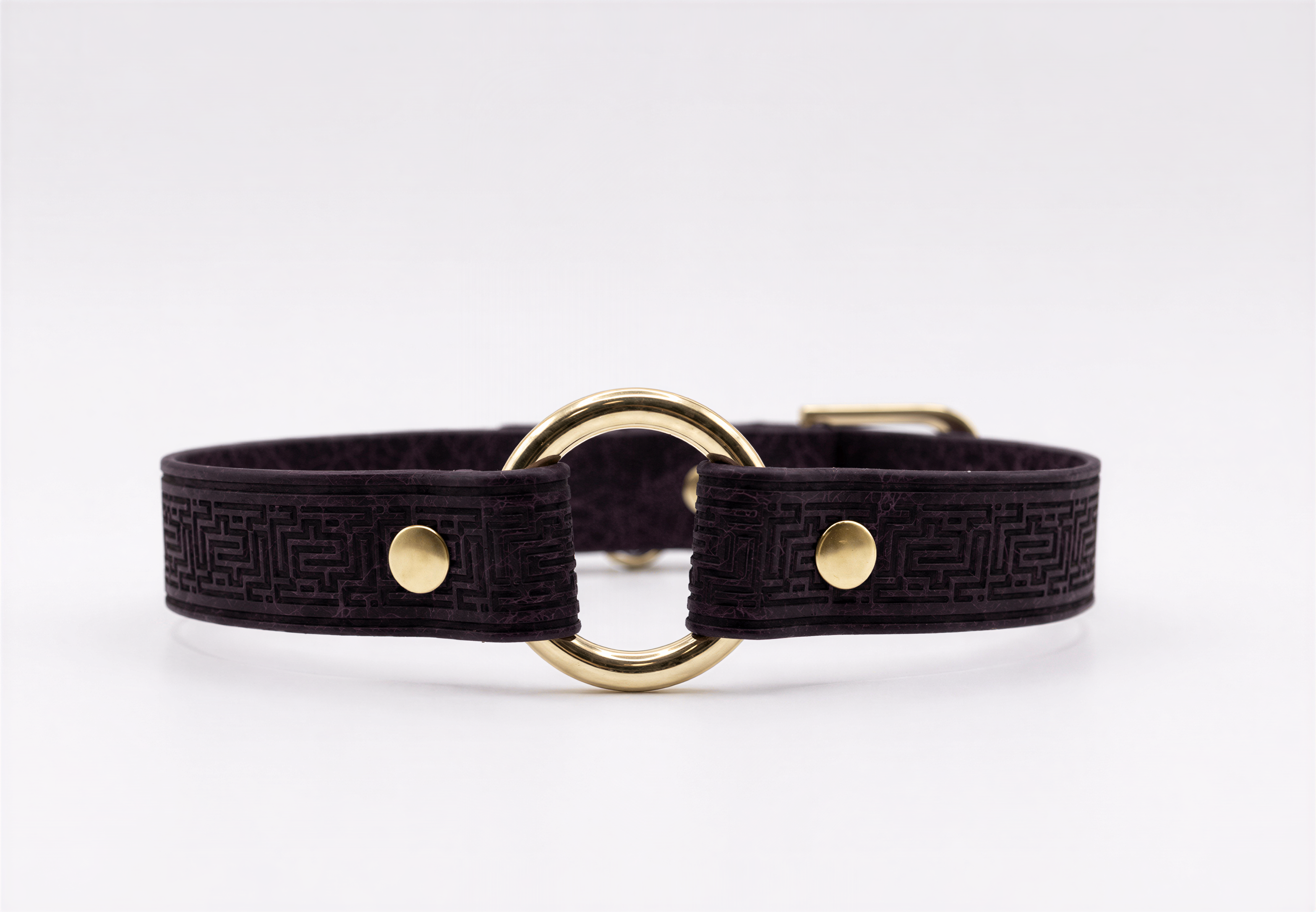 A dark purple leather collar with a gold-colored metal ring and two gold-colored metal fasteners.