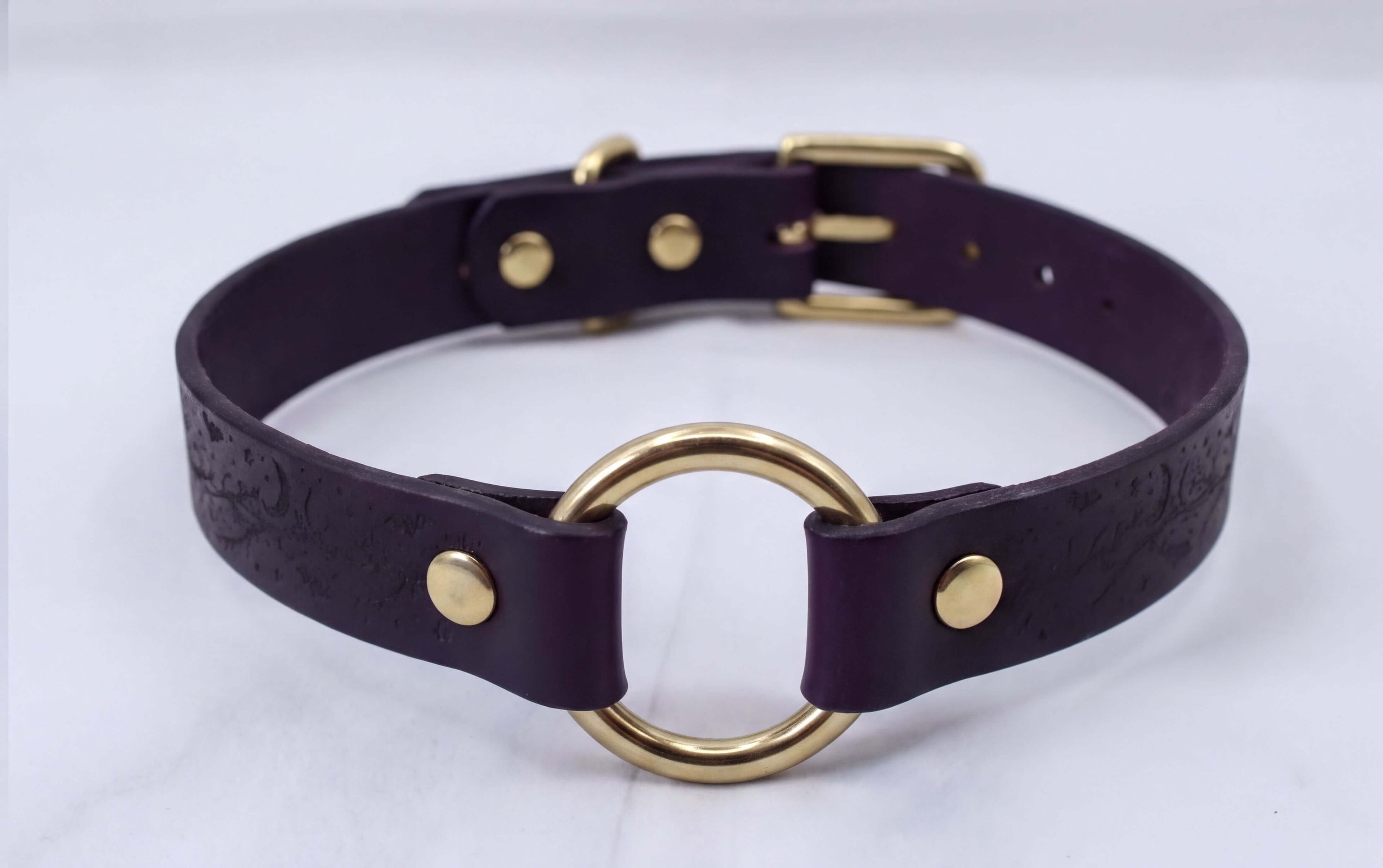 A purple leather choker collar with a gold ring and buckle.