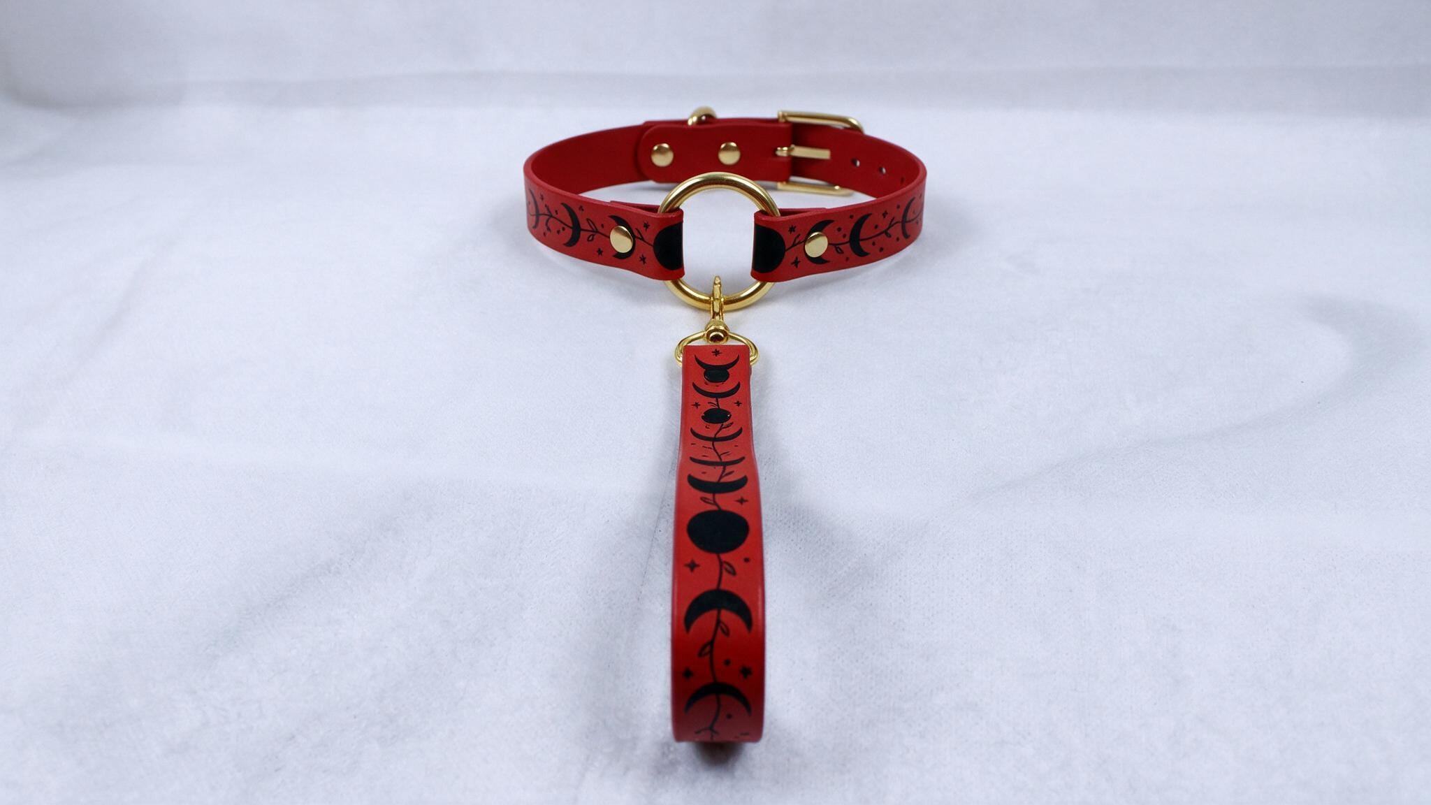A red collar with a gold buckle and a black and white pattern on the strap is displayed against a white background.