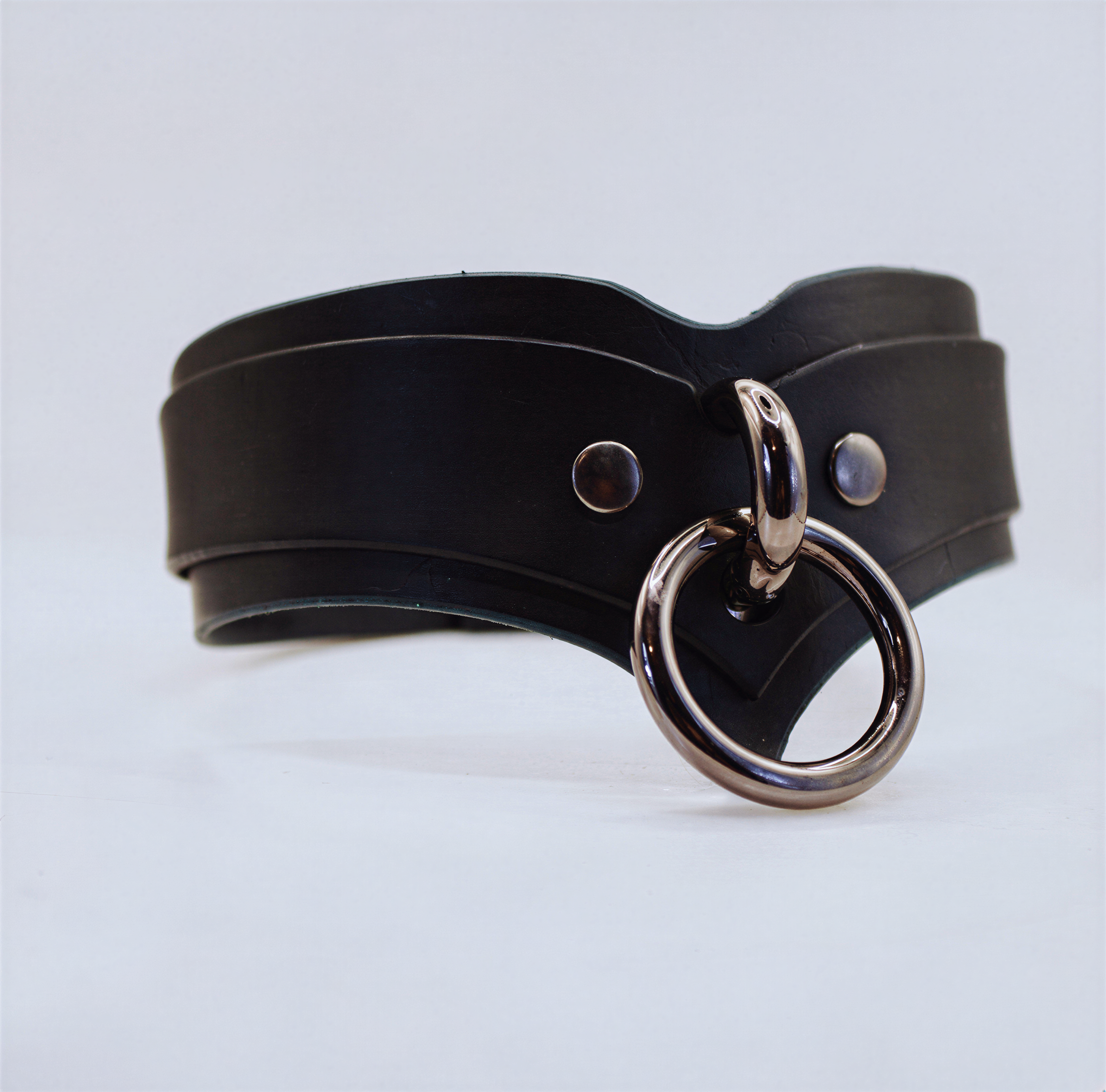 A black leather choker necklace with a metal ring and two metal studs on the front.