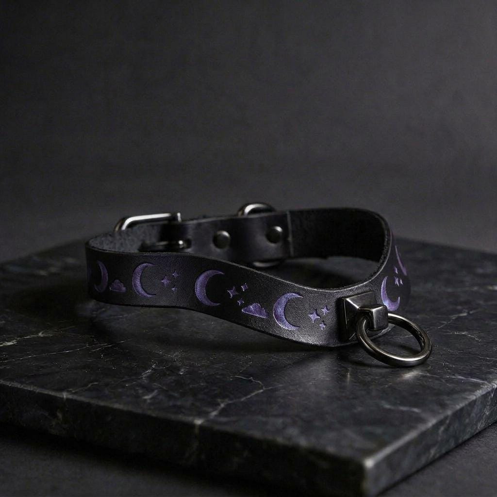 A black leather collar with purple moon and star designs on a dark background.
