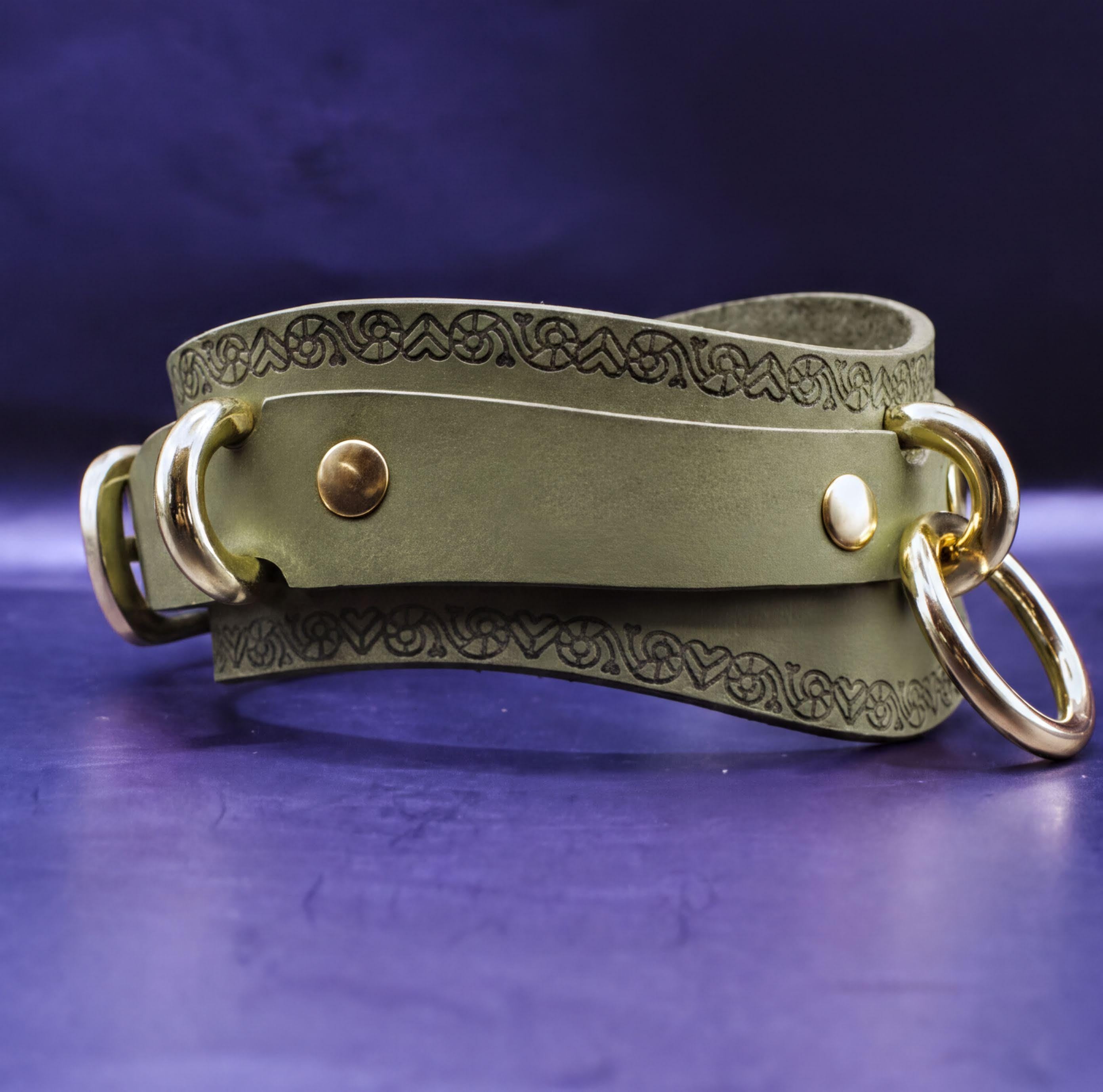 A green leather choker necklace with a decorative pattern and two gold-colored metal rings on either side.