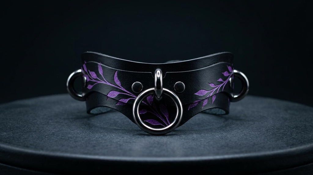 A black leather collar with purple leaf designs and metal rings on the front.