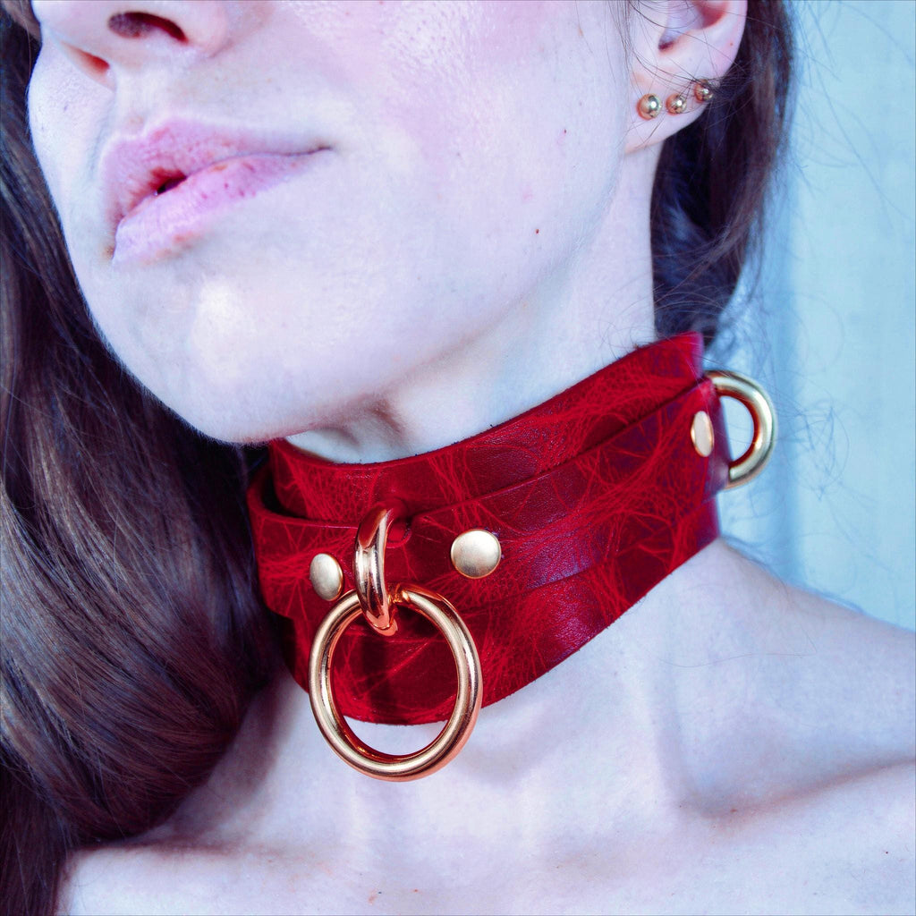 A close-up of a person's neck and chest area wearing a red choker necklace with gold-colored metal rings.