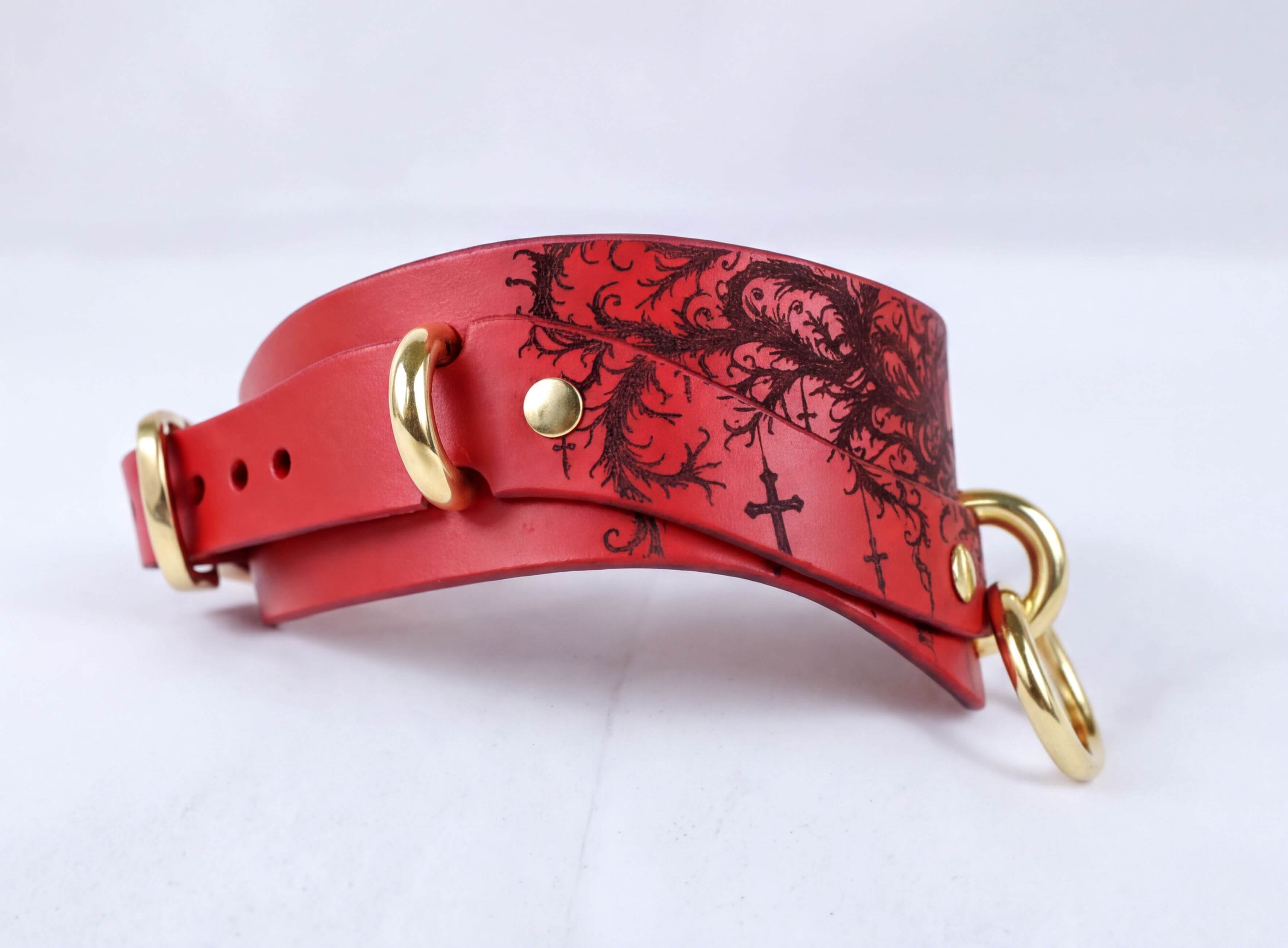 A red leather collar with a black floral design and gold hardware.