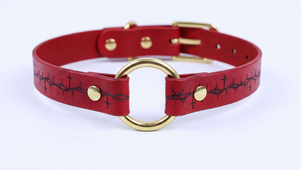 A red leather choker collar with a gold-colored metal ring and a black design on the front.