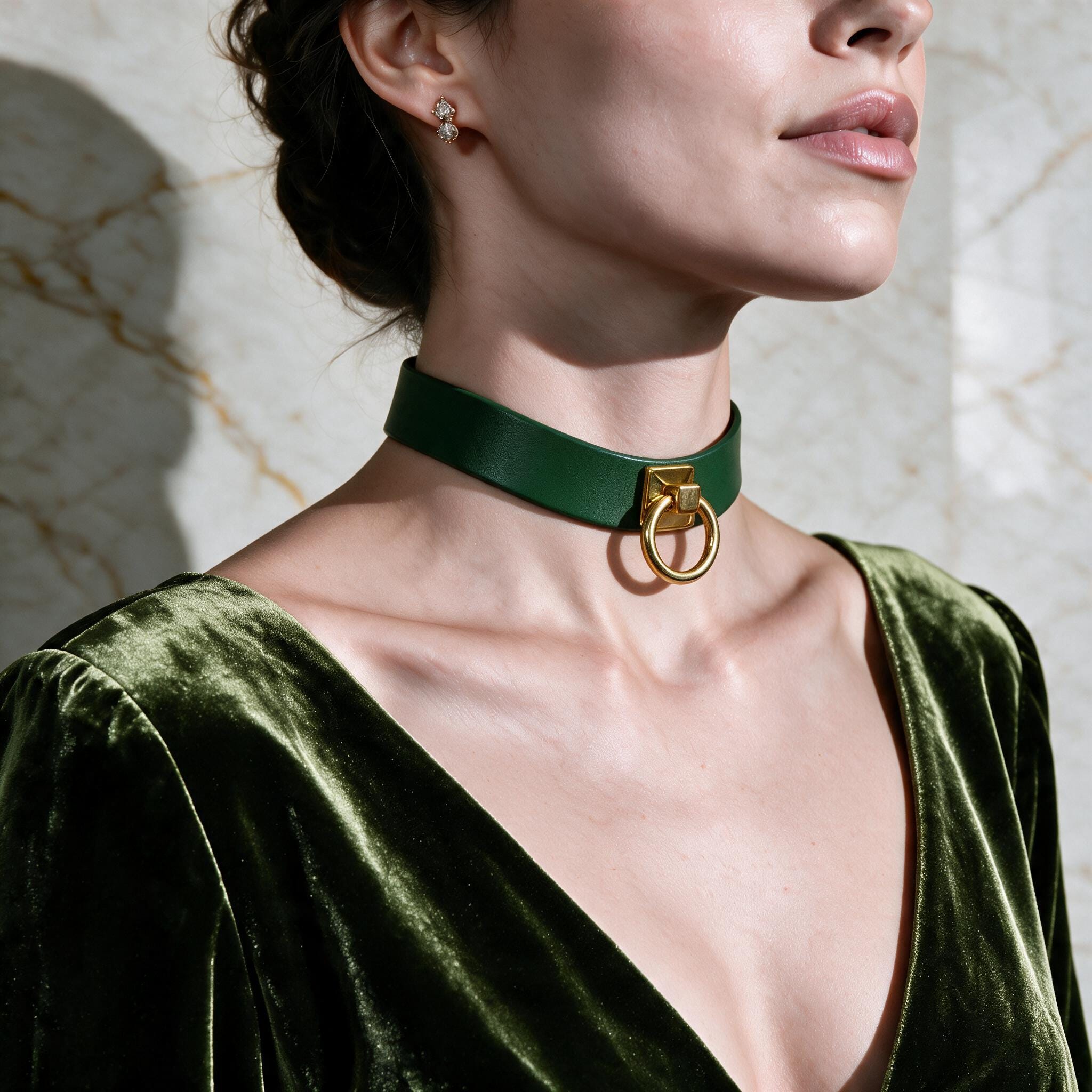 A woman wearing a green choker necklace with a gold ring on it, posing against a marble wall.