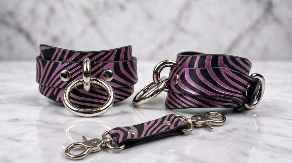 a pair of zebra-striped leather straps with metal rings and buckles, arranged on a marble surface.