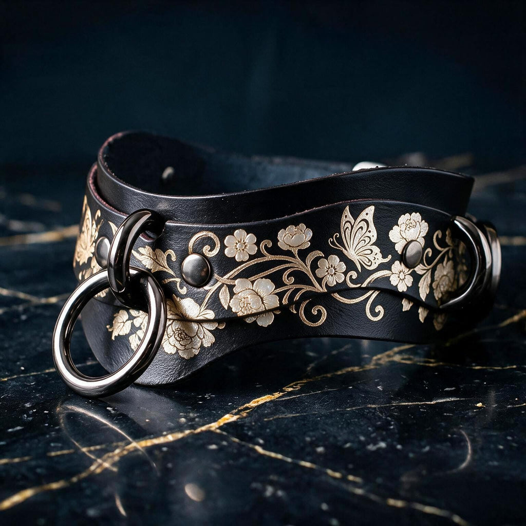 A black leather strap with a floral pattern and metal rings on it, resting on a dark surface.