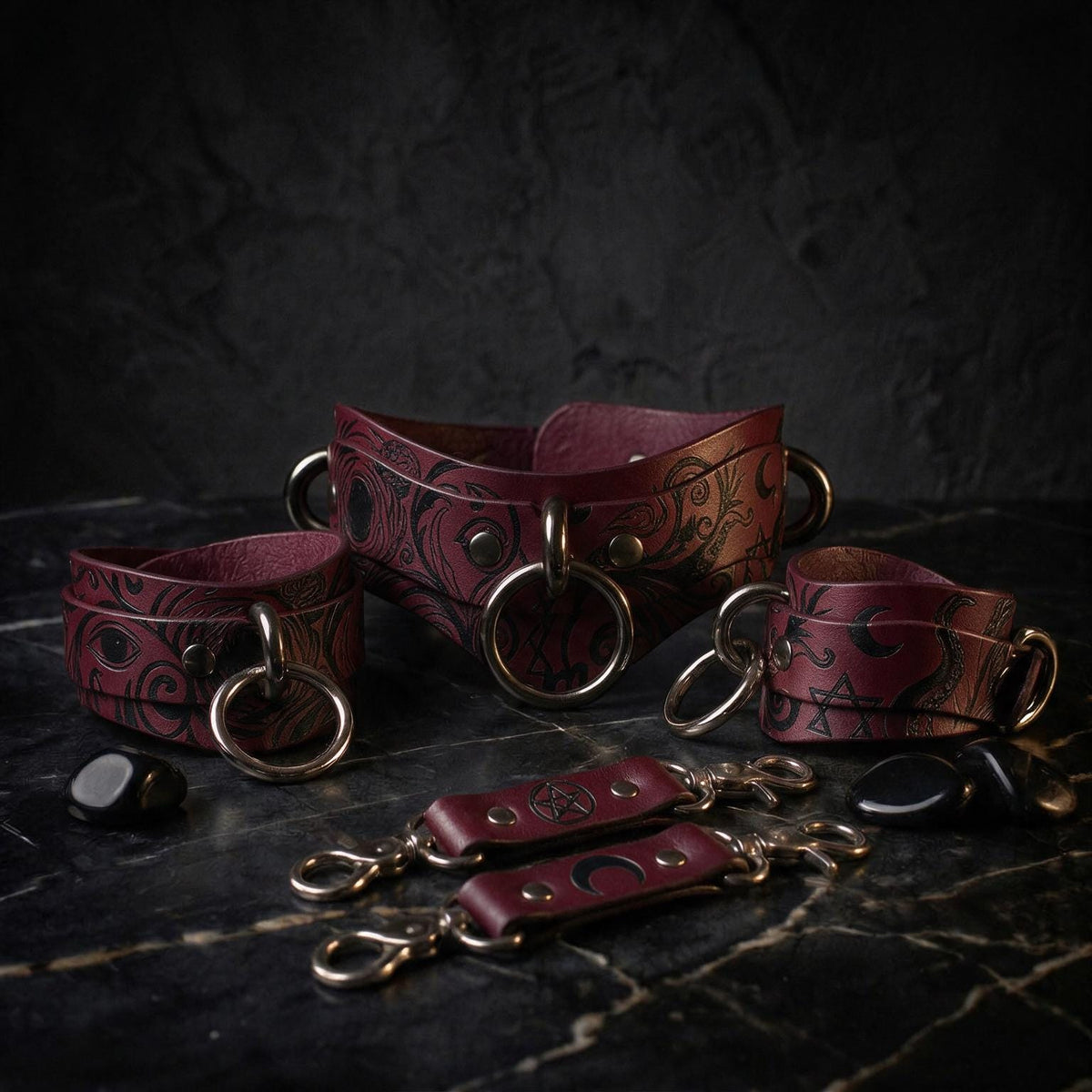 A collection of burgundy leather straps with metal rings and buckles, arranged on a dark surface.