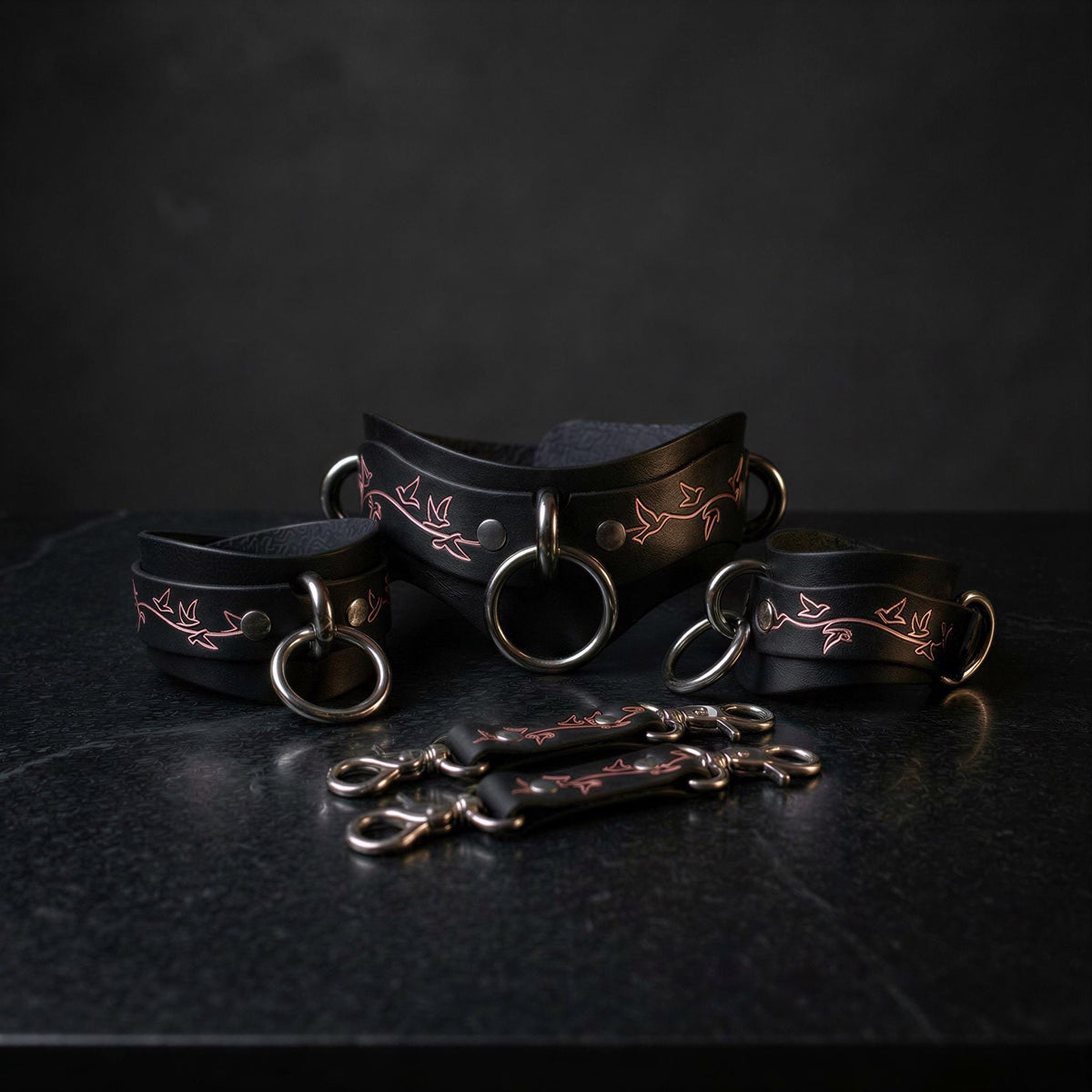 a set of black leather straps with metal rings and buckles, arranged on a dark surface.