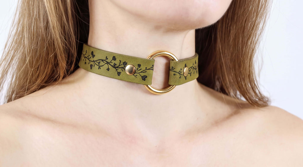 A close-up of a woman's neck wearing a green choker necklace with a gold ring.
