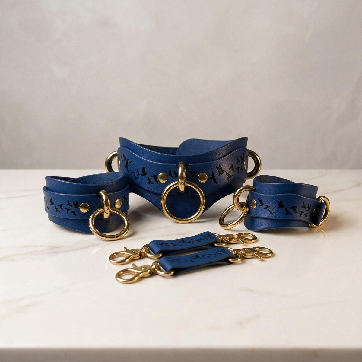 A set of blue leather straps with gold rings and buckles, arranged on a white marble surface.