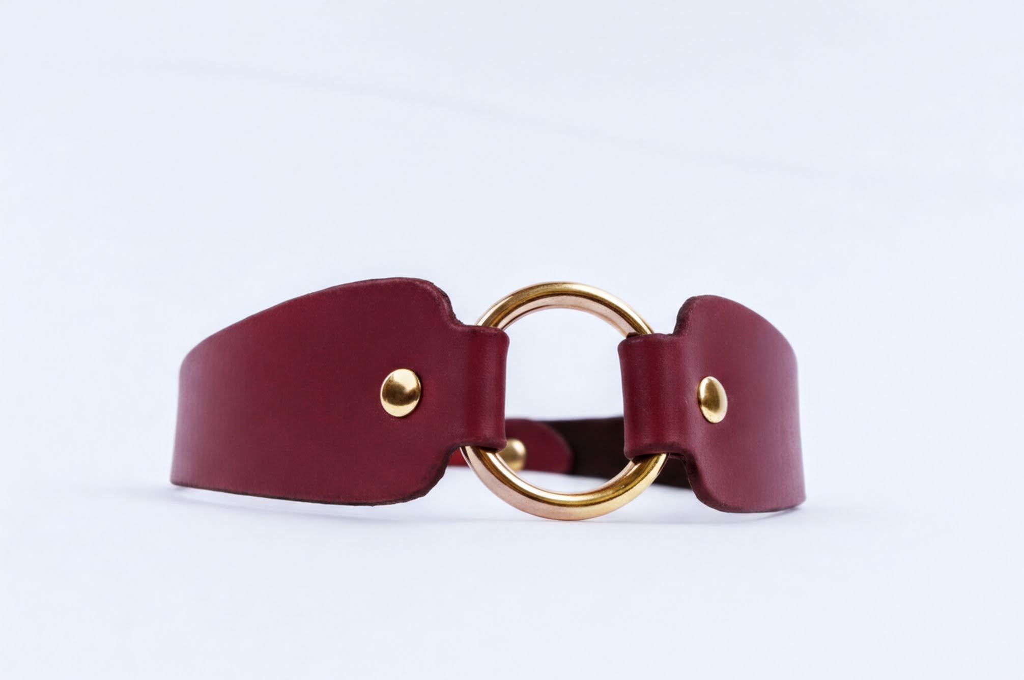 A burgundy leather choker necklace with a gold-colored circular buckle.