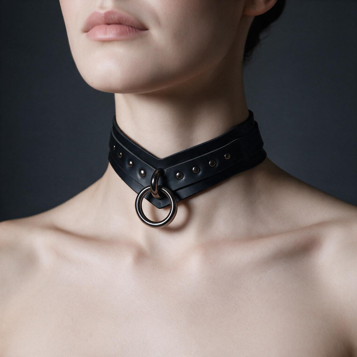 A close-up of a woman's neck wearing a black leather choker necklace with a metal ring.