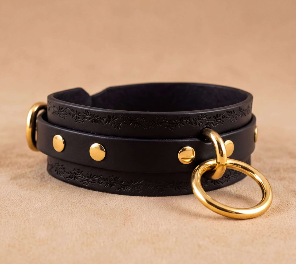 A black leather choker necklace with gold-colored metal rings and studs, resting on a beige background.