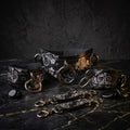 a collection of ornate leather straps and buckles, including a large black strap with a floral pattern and smaller straps with similar designs. The straps are arranged on a dark surface, with some of them lying on the ground.