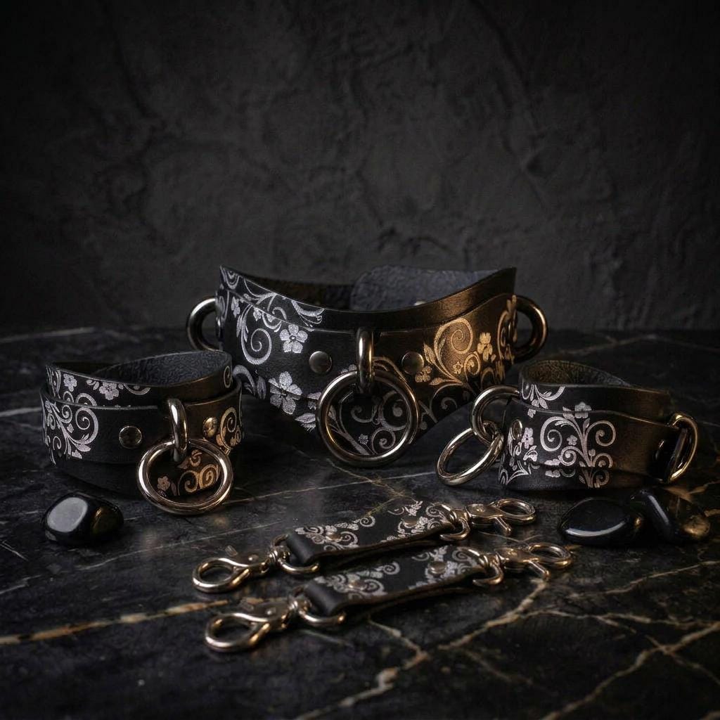 a collection of ornate leather straps and buckles, including a large black strap with a floral pattern and smaller straps with similar designs. The straps are arranged on a dark surface, with some of them lying on the ground.