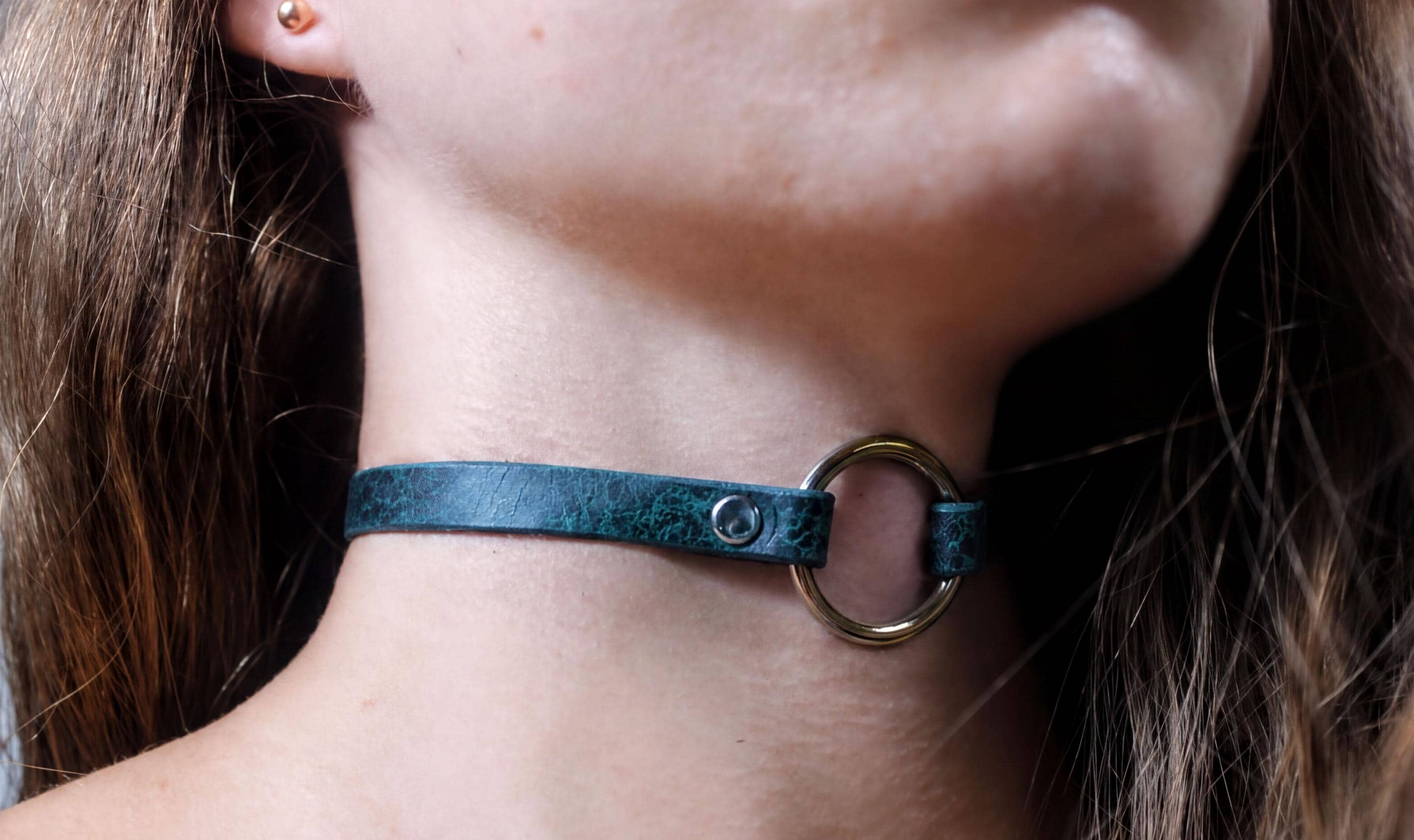 A close-up view of a person's neck and chin area, featuring a green leather choker necklace with a metal ring.