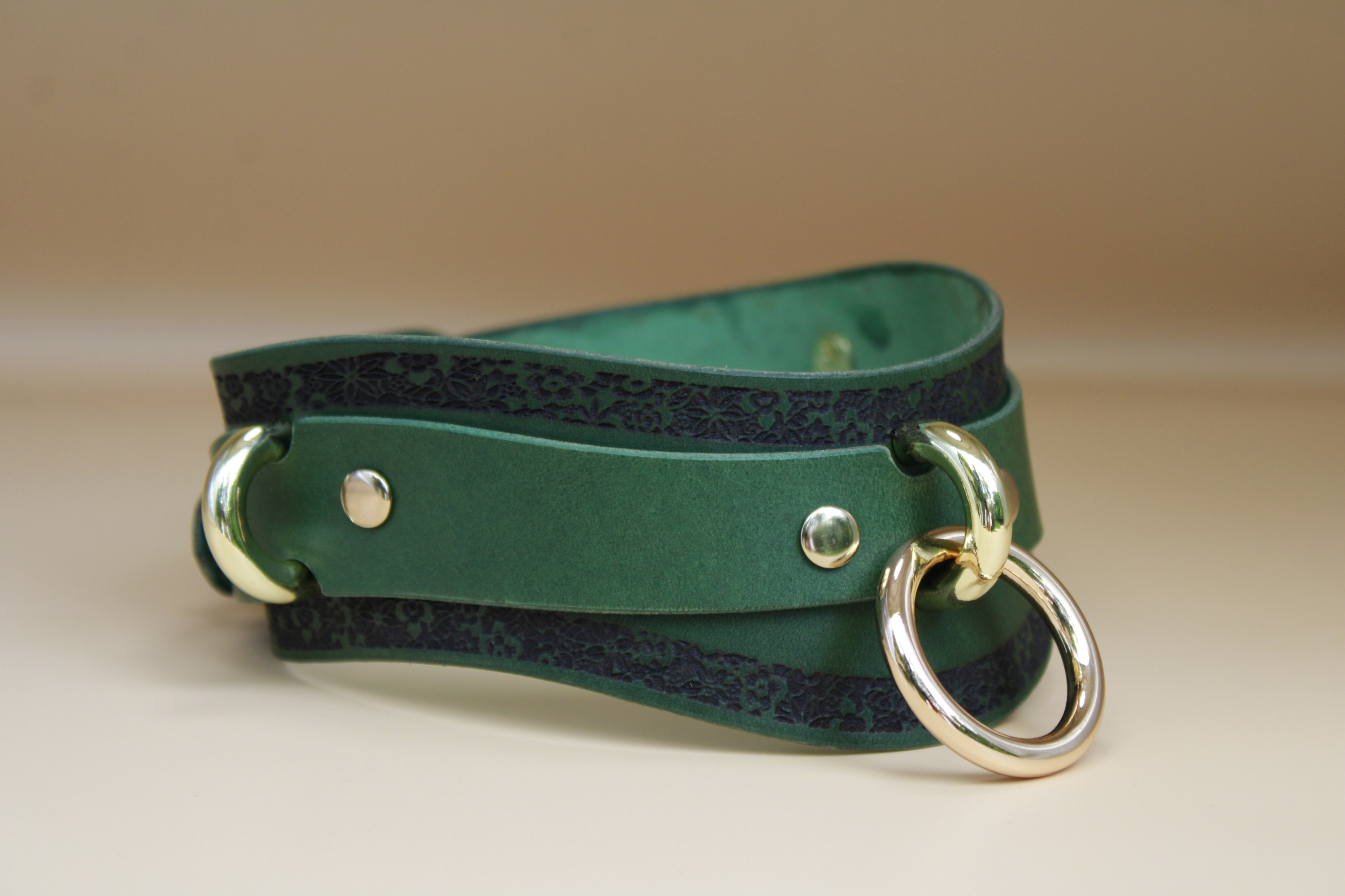 A green leather choker necklace with a gold-colored metal ring and two metal rings on either side.