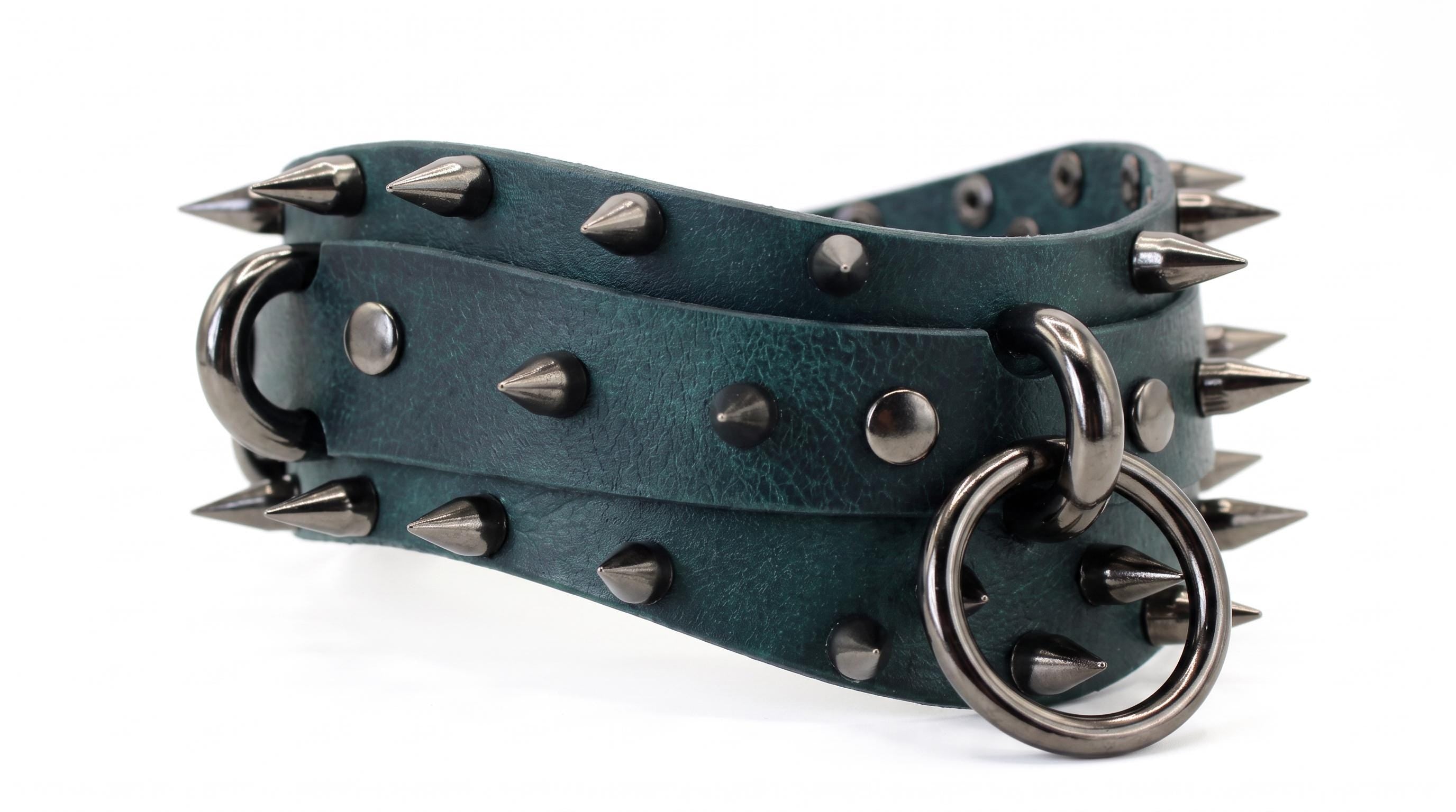 A close-up image of a green leather belt with spikes and metal rings.