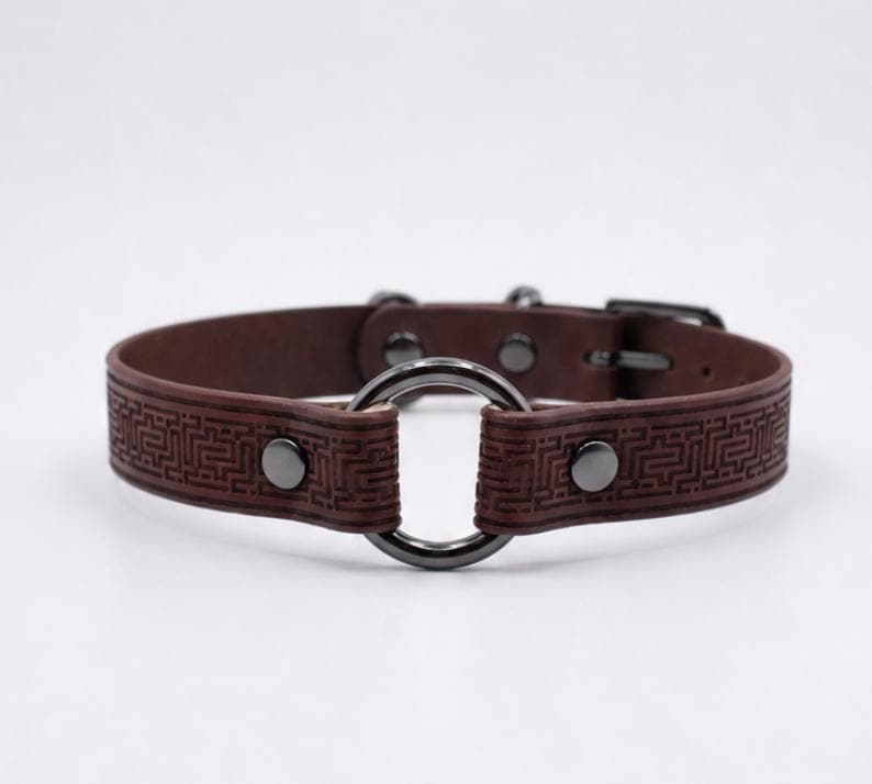 A brown leather collar with a metal ring and buckle.