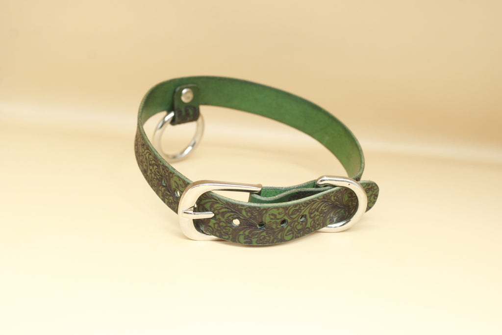 A green leather collar with a silver buckle is shown against a beige background.