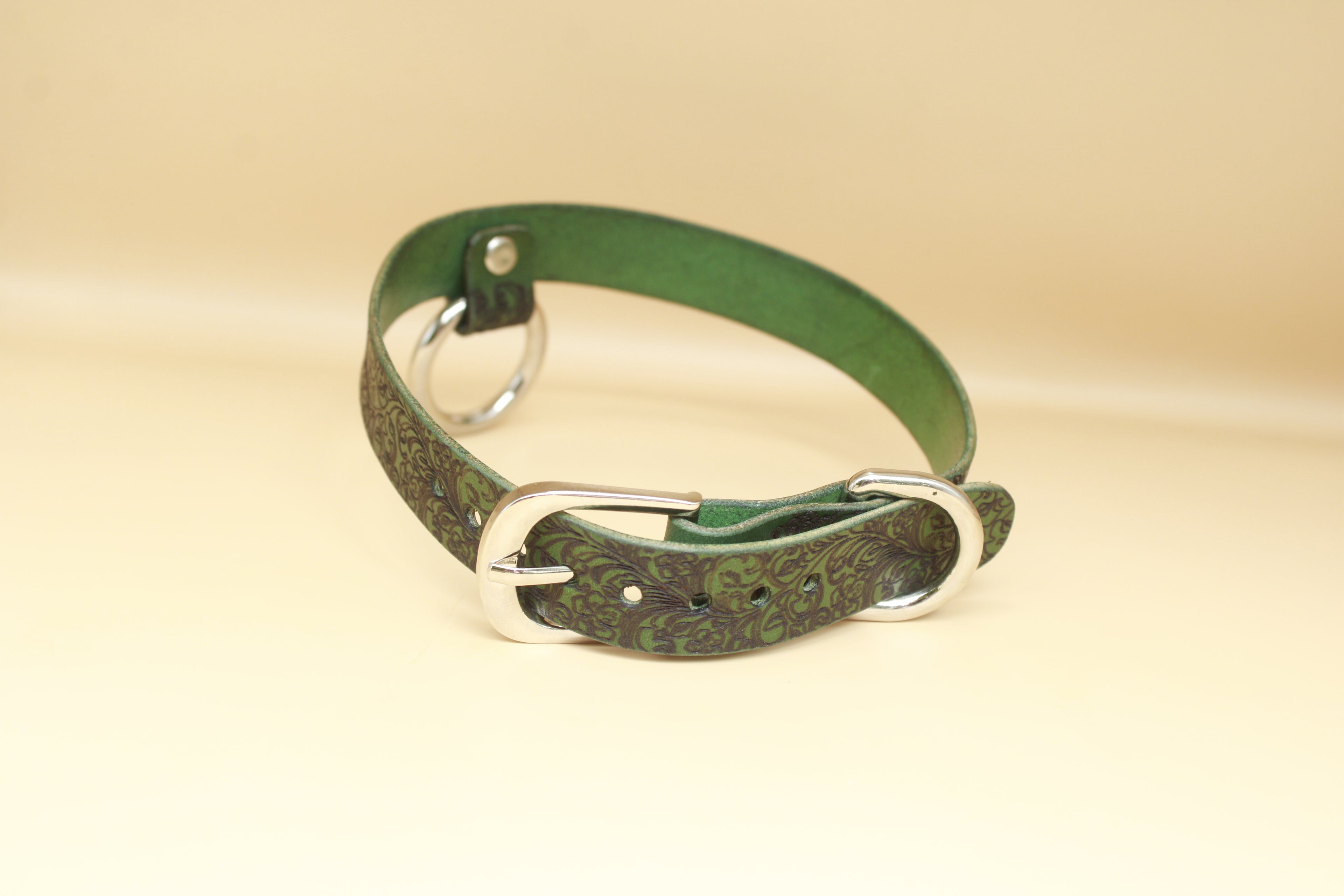 A green leather collar with a silver buckle is shown against a beige background.